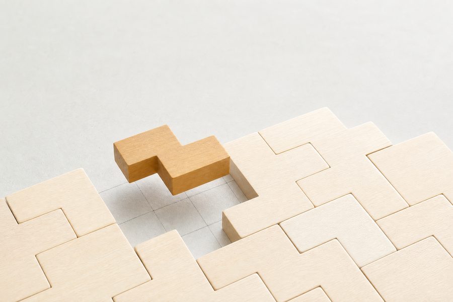 Pale wooden interlocking puzzle blocks on a light surface with one piece lifted out of place